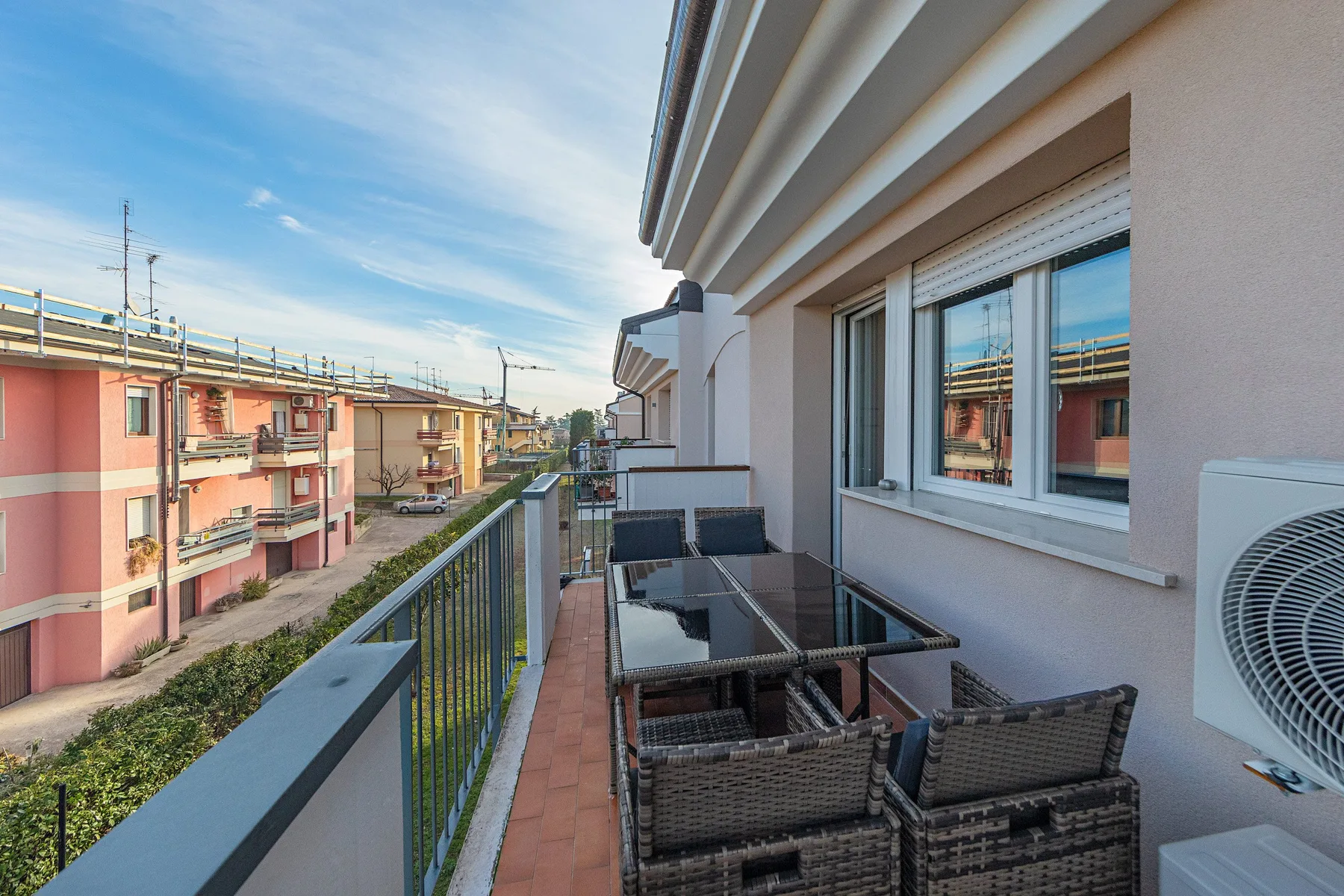 A balcony seating area with a glass table overlooks neighboring buildings.