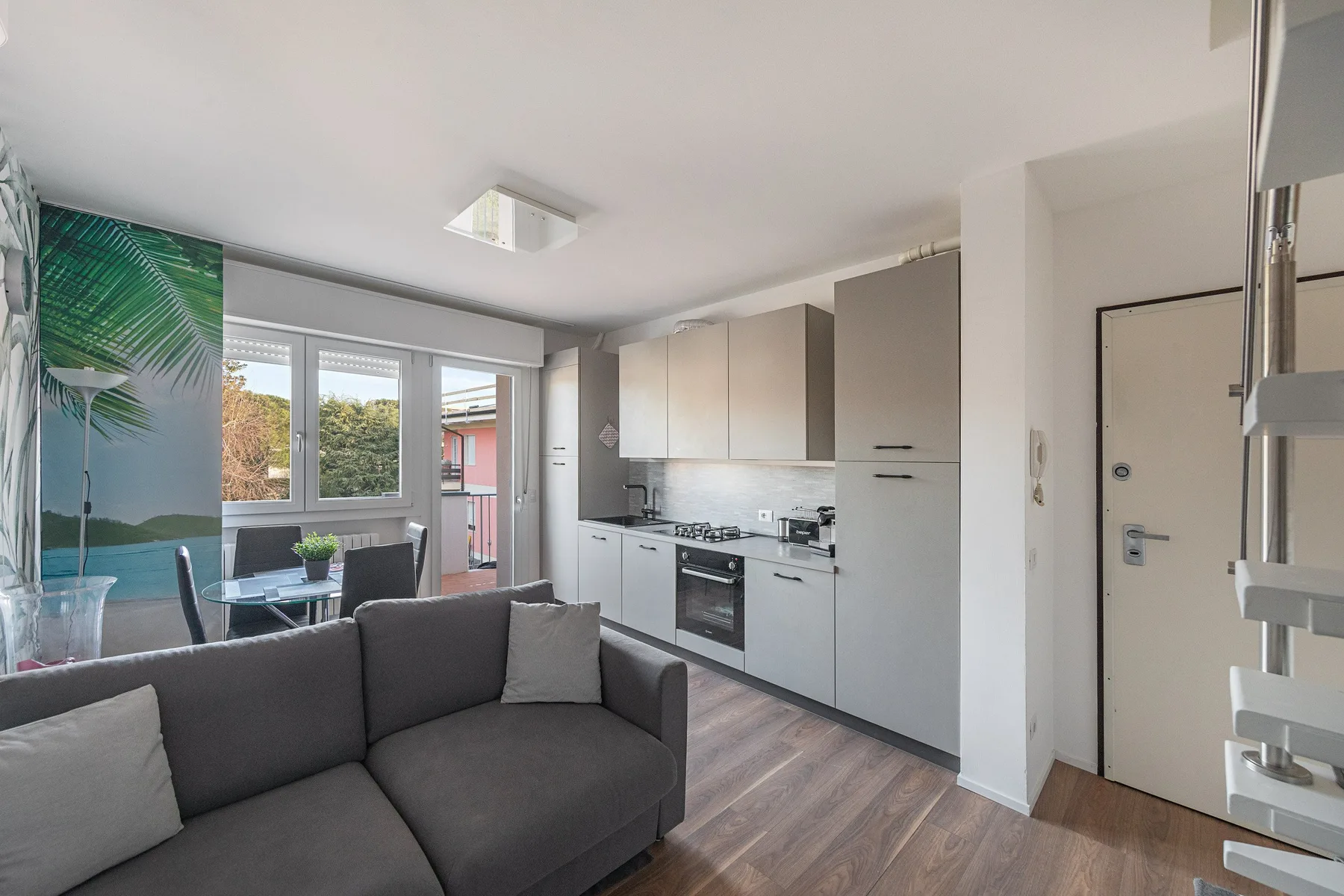 Living room and kitchen with gray seating, cabinets, and windows.