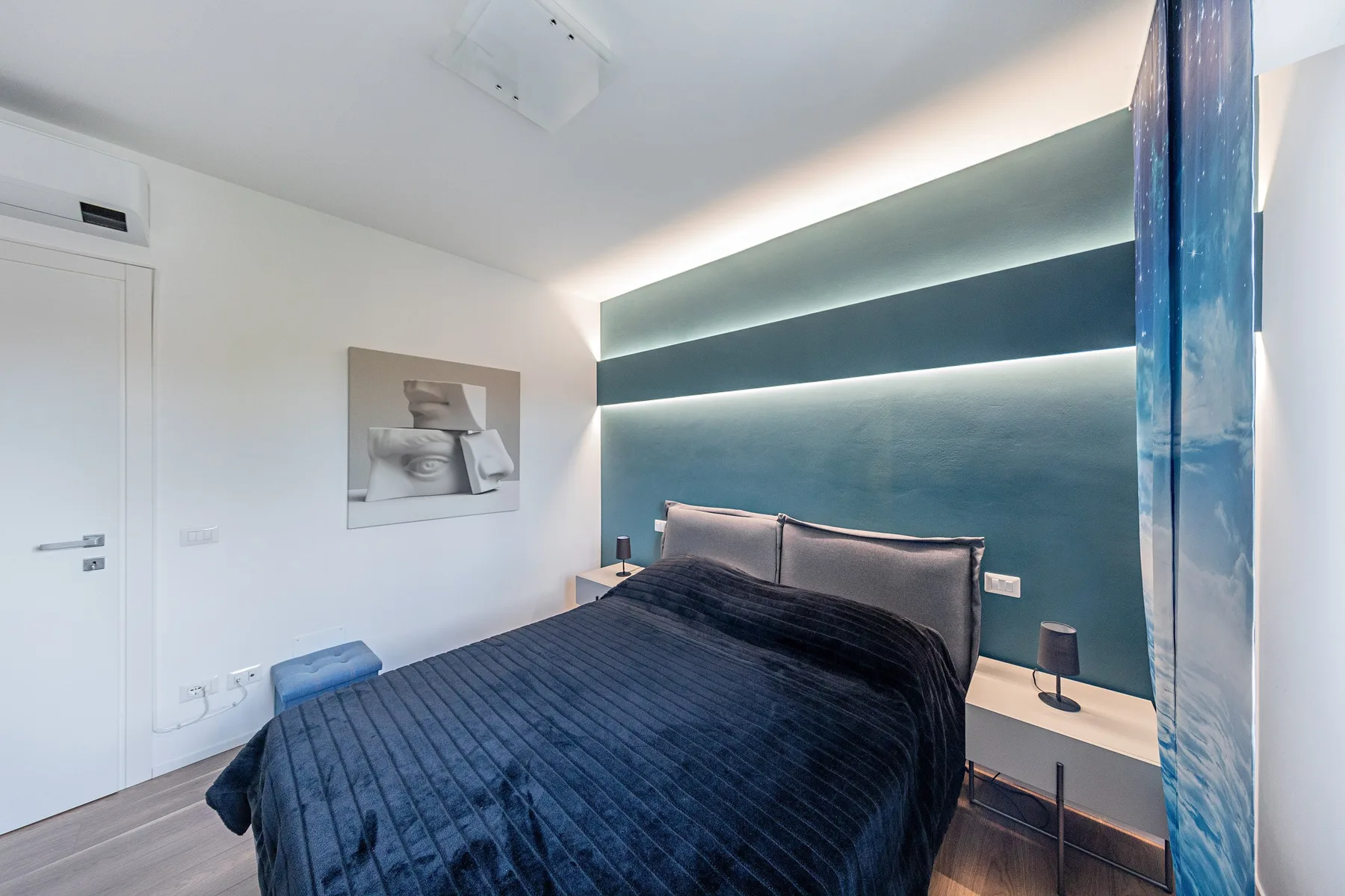 A bedroom with a bed against a dark teal accent wall.