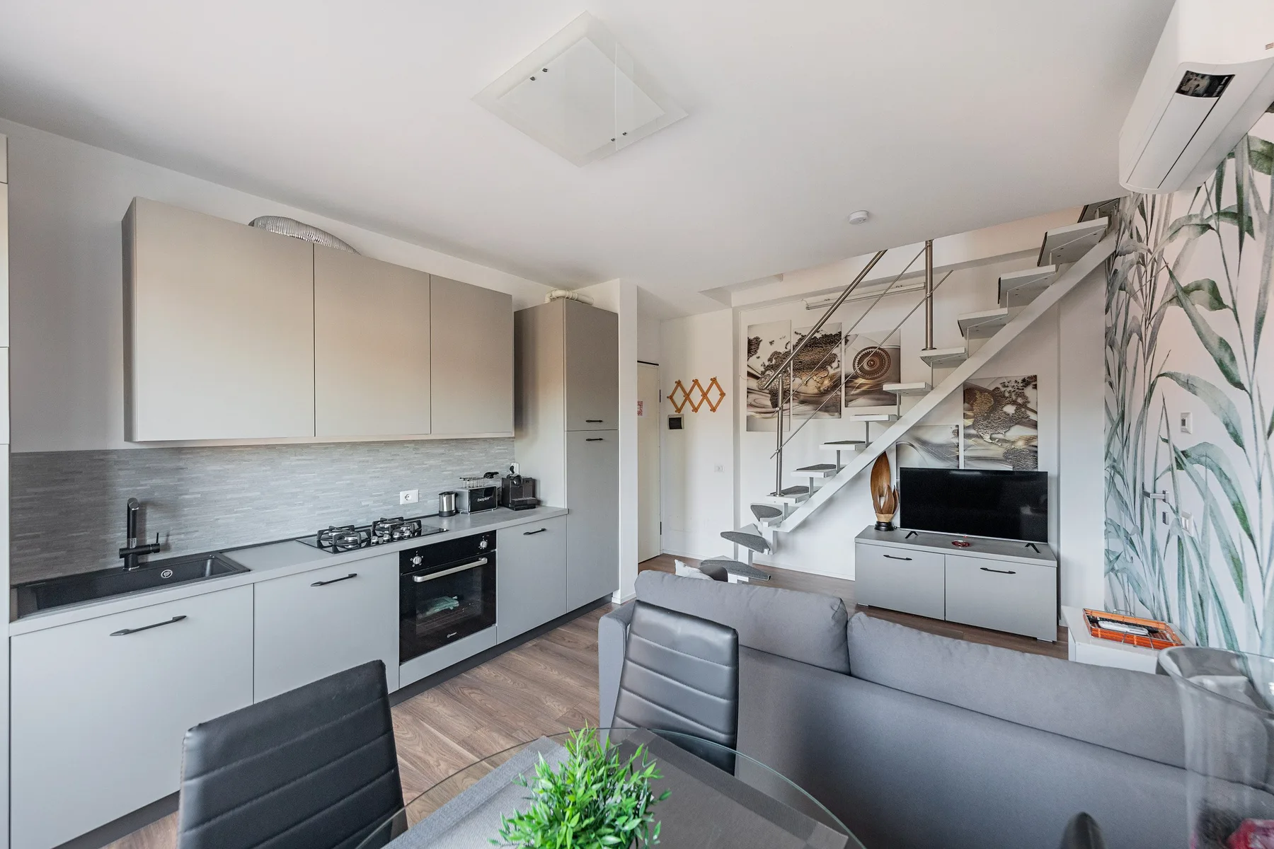 A modern open-plan living area with a kitchen, seating, and stairs.