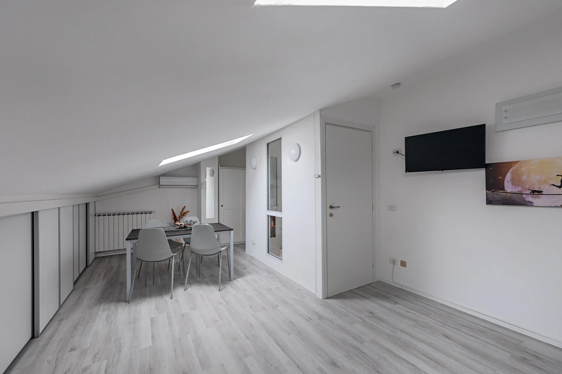 A bright dining area with a table and seating beneath a sloped ceiling.