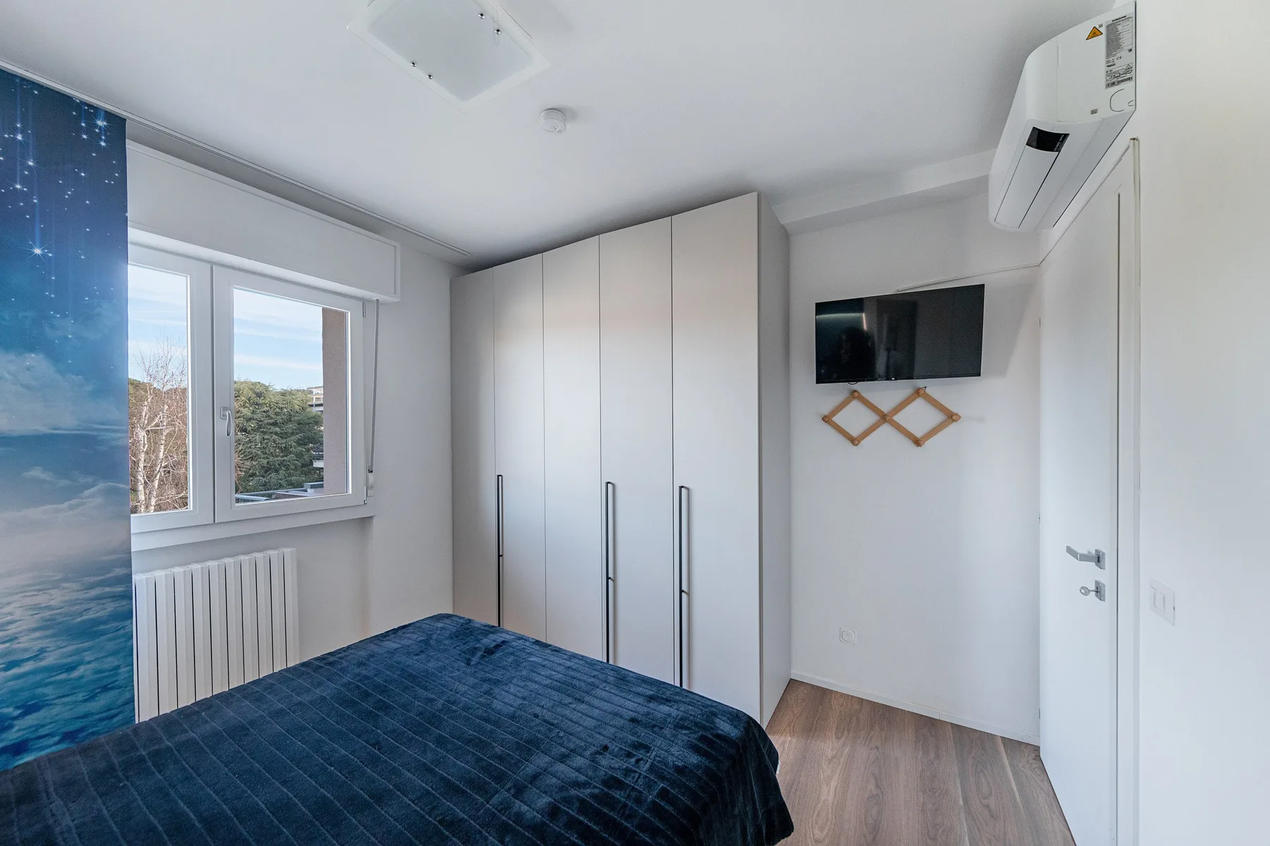 A bedroom with a bed, wardrobe, and window overlooking trees.