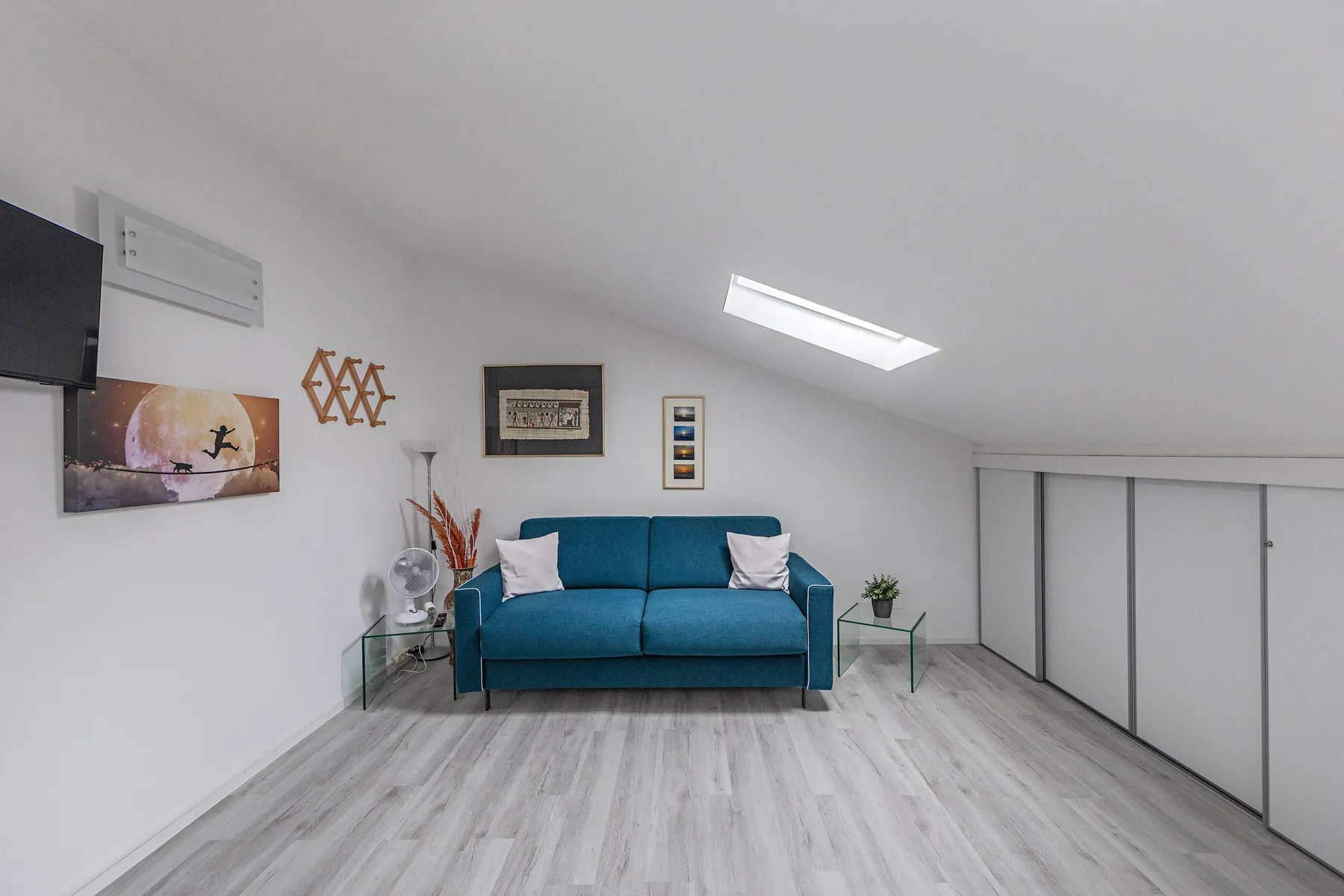 A bright attic living area with a blue sofa beneath a sloped ceiling.
