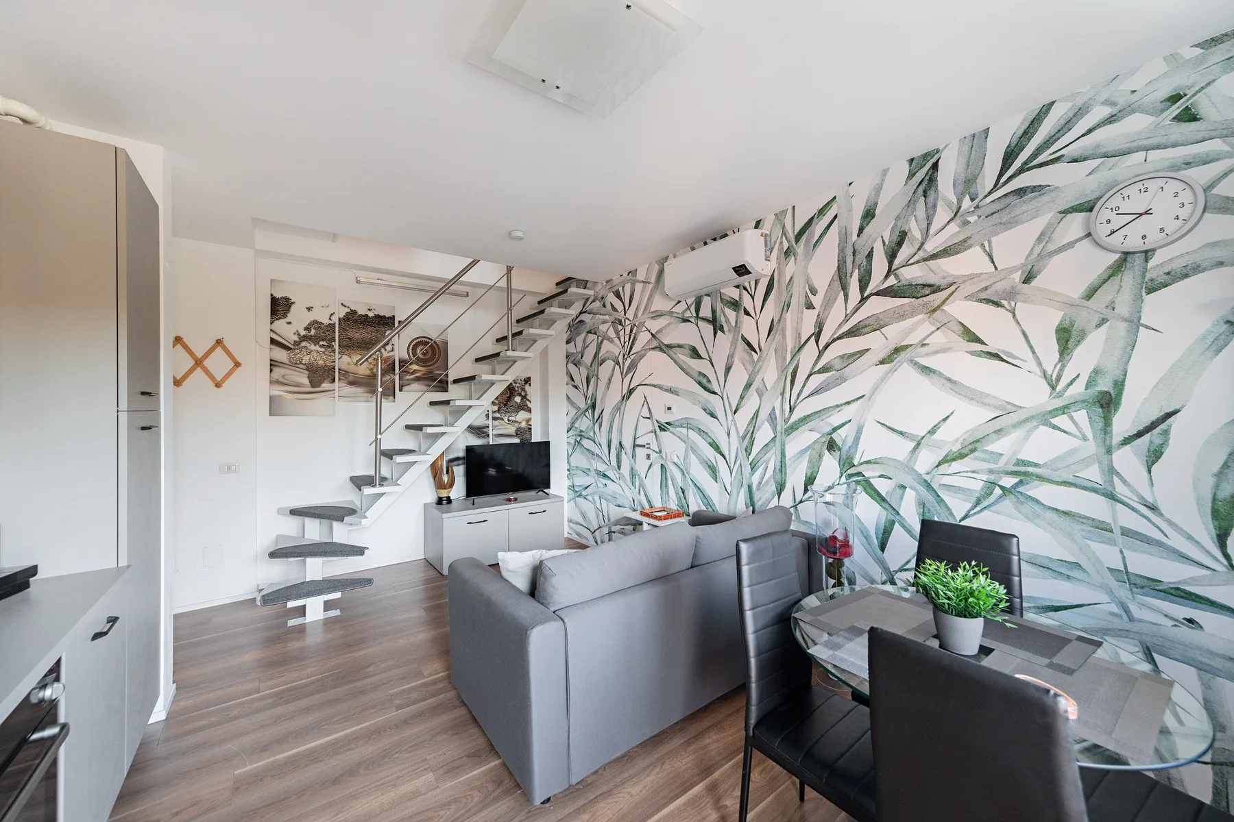 A living and dining area with gray seating and a leafy wall mural.