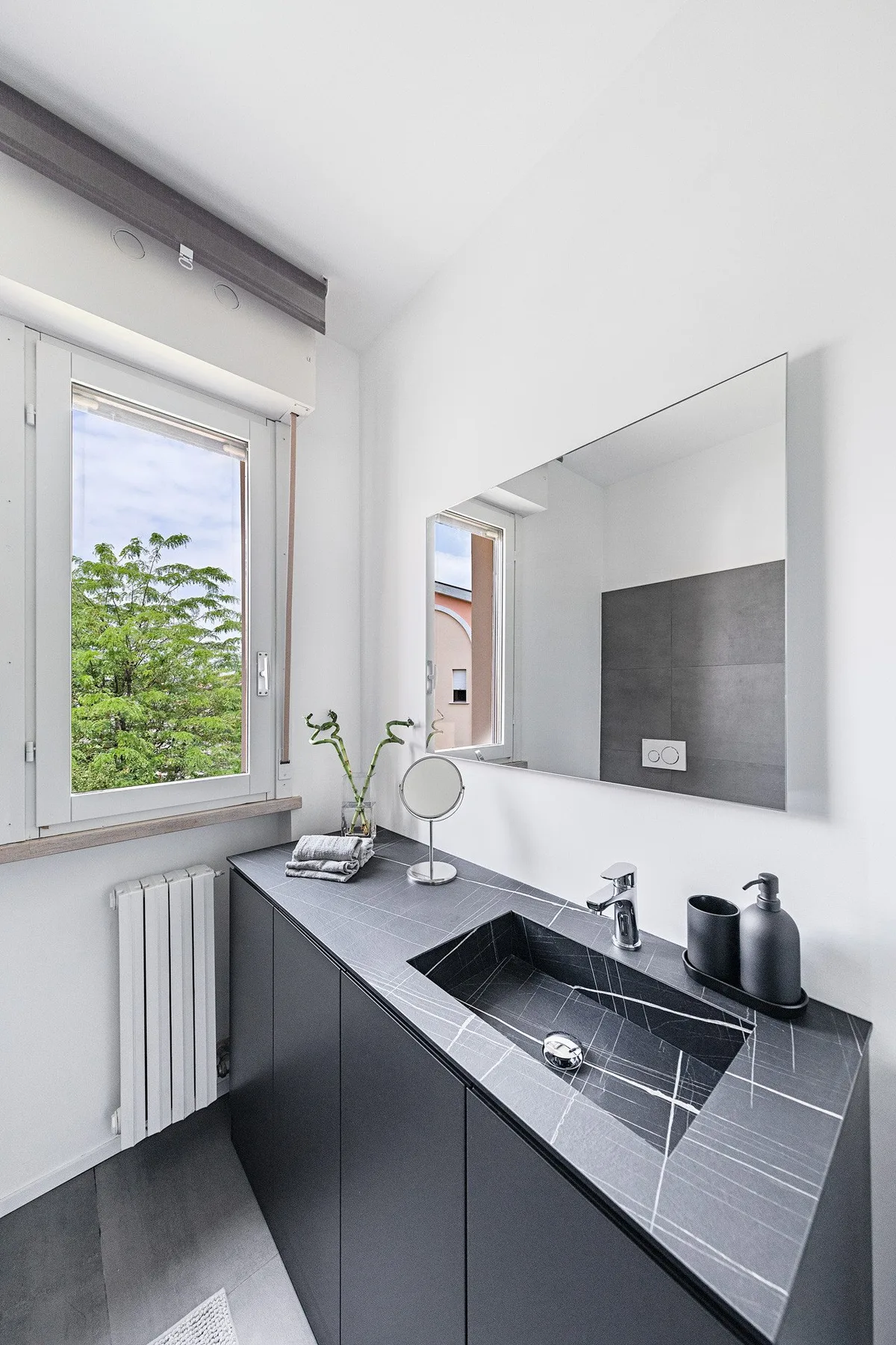 A modern bathroom with a dark vanity, integrated sink, and large mirror.