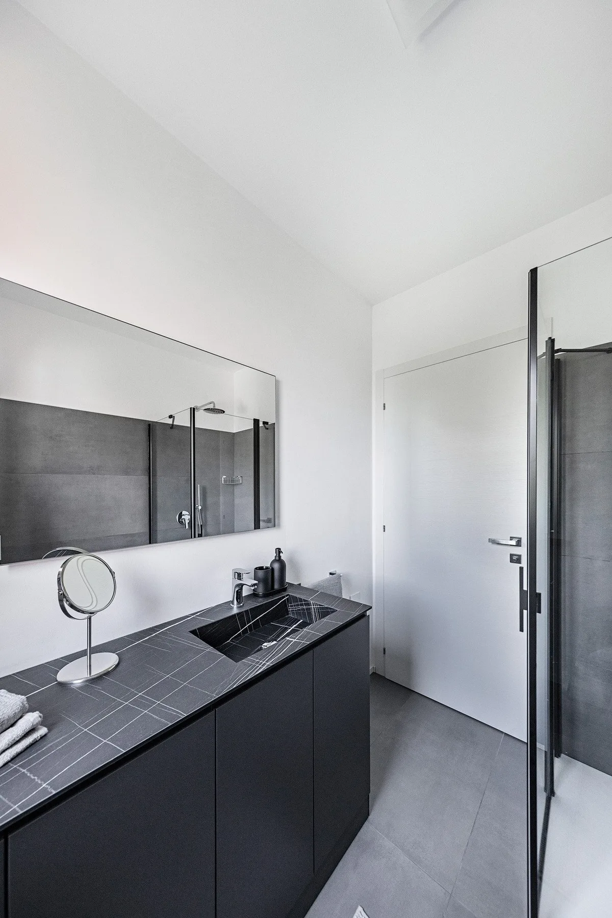 A modern bathroom vanity with a dark countertop, wall mirror, and shower.