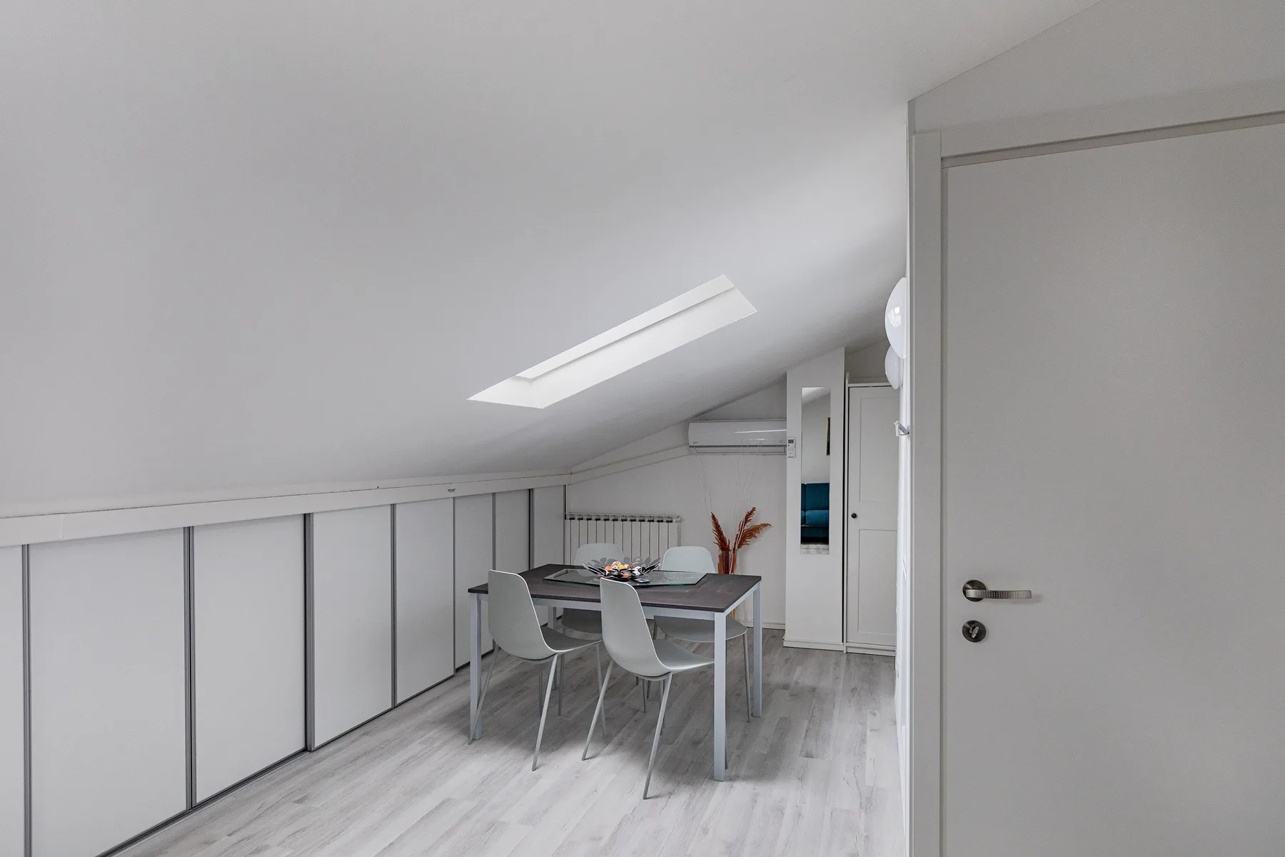 A bright dining area under a sloped ceiling, with a table and seating.