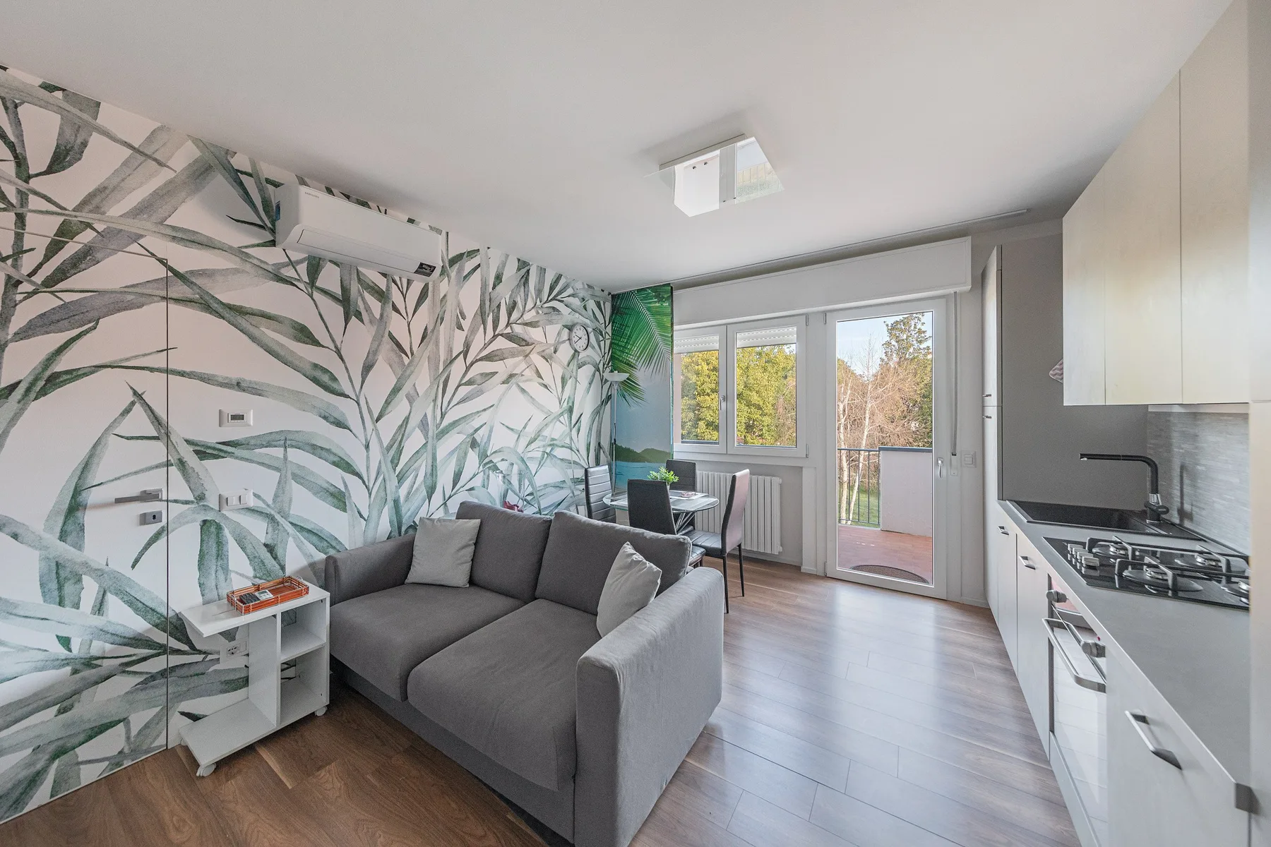 A compact living area with gray seating beside a kitchen and glass doors.