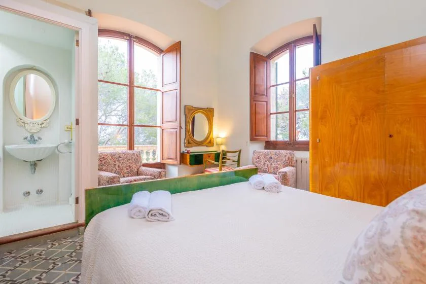 Un dormitorio con una cama grande, ventanas altas y una puerta abierta al baño.