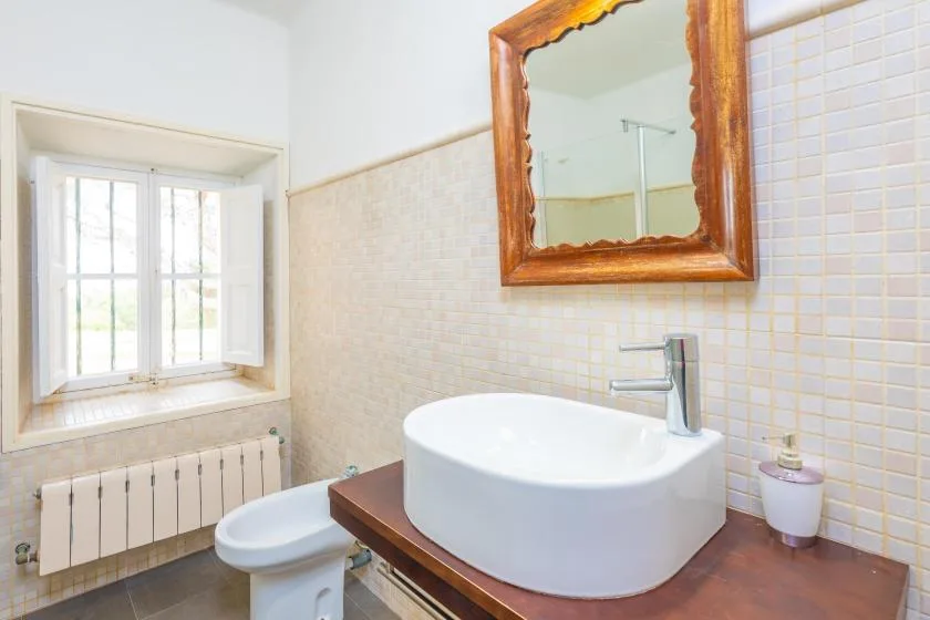 Un baño con lavabo sobre encimera, espejo y ventana.