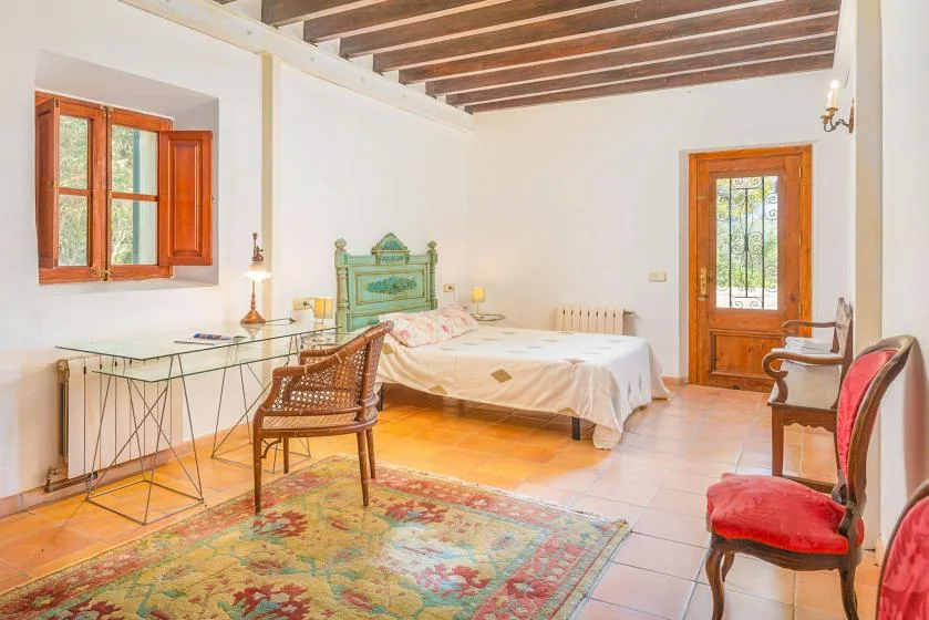 Un dormitorio con una cama, un escritorio y ventanas con marcos de madera.