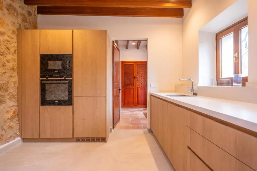 Una cocina luminosa con gabinetes de madera, horno empotrado y una encimera larga.