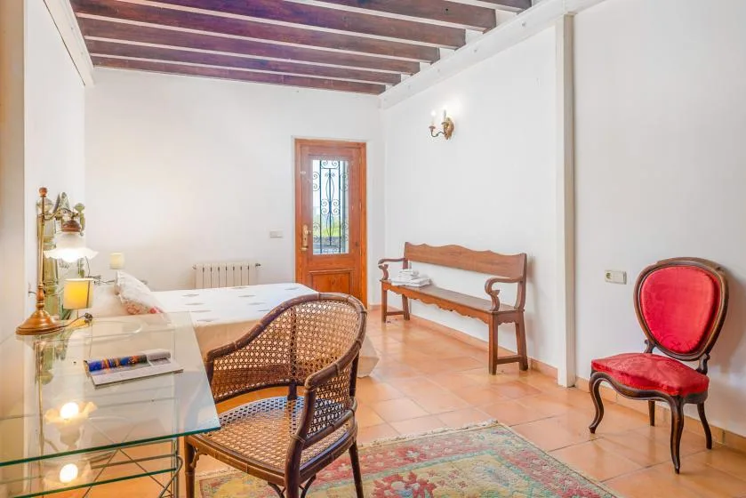 Un dormitorio luminoso con una cama, asientos de mimbre y un banco de madera.