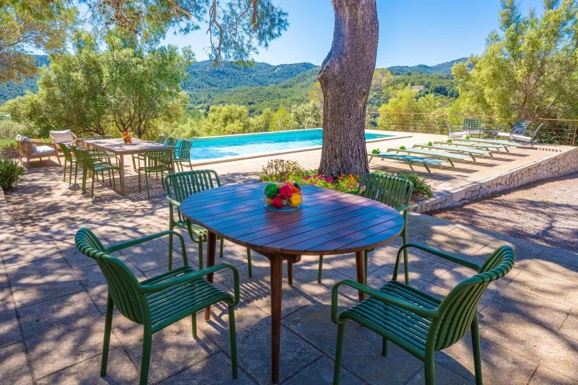 Una zona de comedor al aire libre da a una piscina y colinas boscosas.