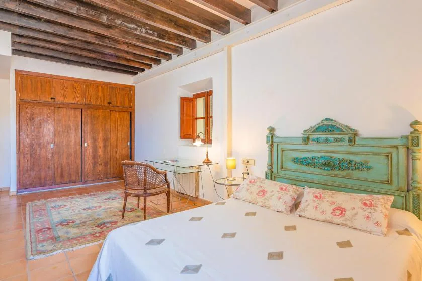 Un dormitorio con una cama, un armario de madera y vigas expuestas en el techo.