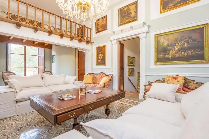 Una sala luminosa con asientos blancos, una mesa de centro de madera y cuadros.