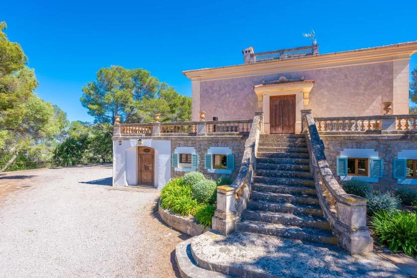 Un edificio de piedra con una escalera exterior, un balcón y árboles alrededor.