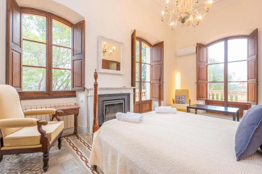 Un dormitorio con una cama grande, una chimenea y ventanas altas.