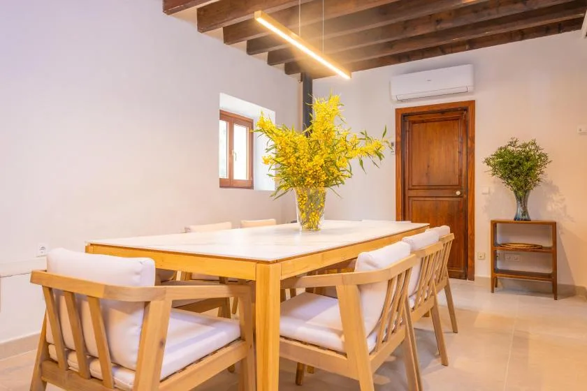 Un comedor con una mesa larga, asientos de madera y flores amarillas.