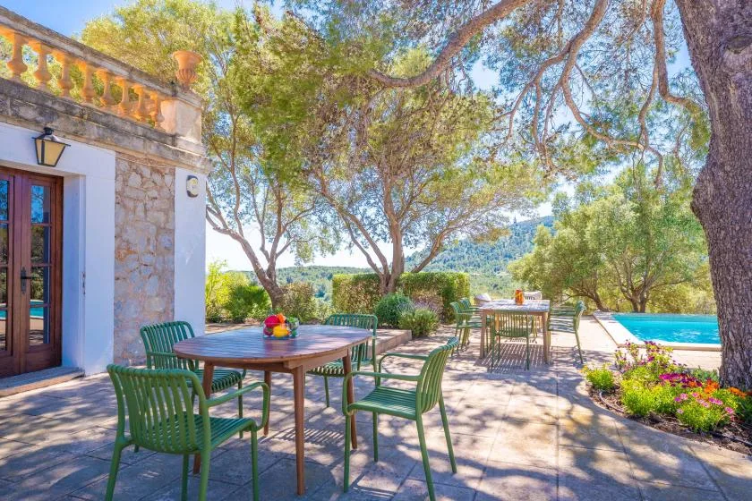 Una zona de comedor al aire libre con asientos verdes junto a un jardín y una piscina.