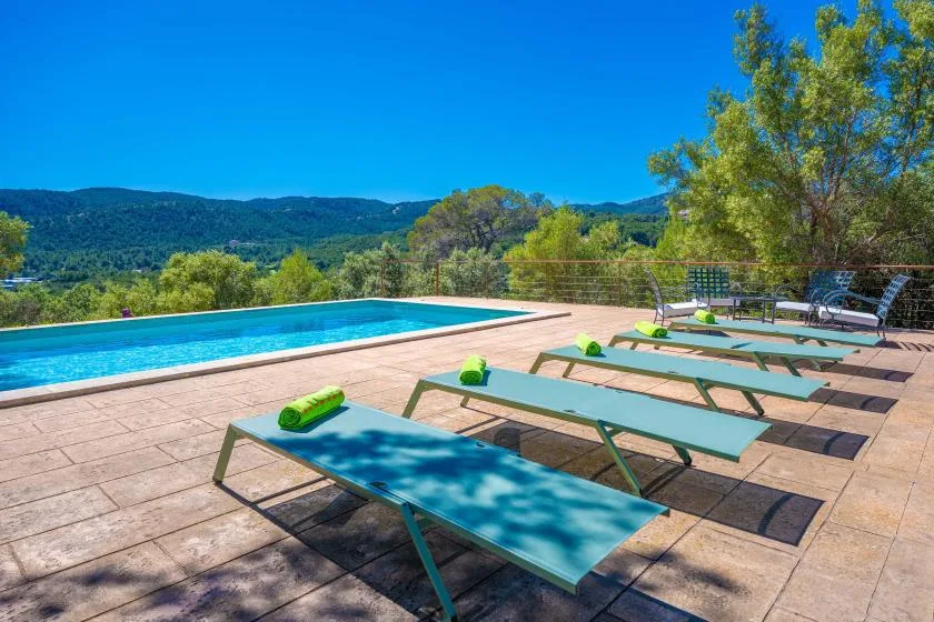 A swimming pool and sun loungers sit on a terrace overlooking green hills.