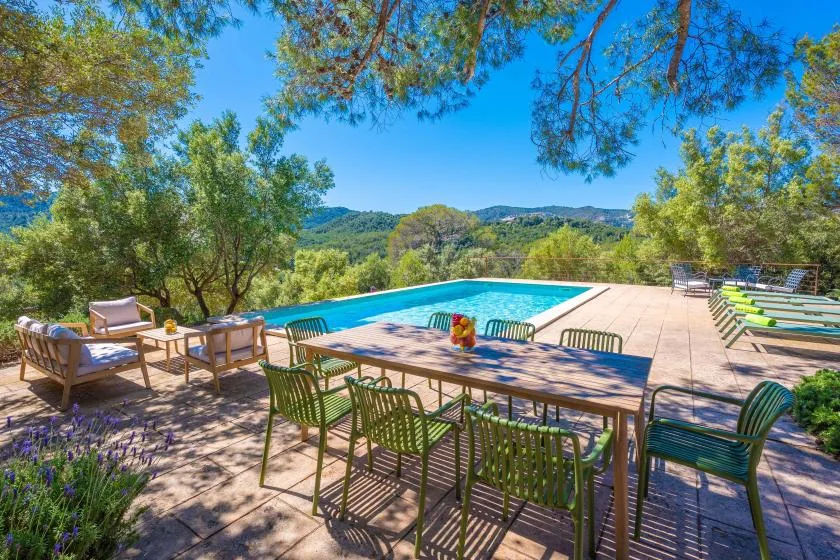 Una zona de comedor al aire libre da a una piscina y colinas verdes.