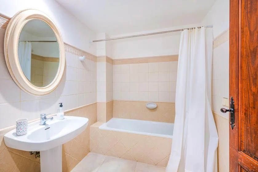 Un baño con azulejos, bañera, cortina blanca y espejo ovalado en la pared.