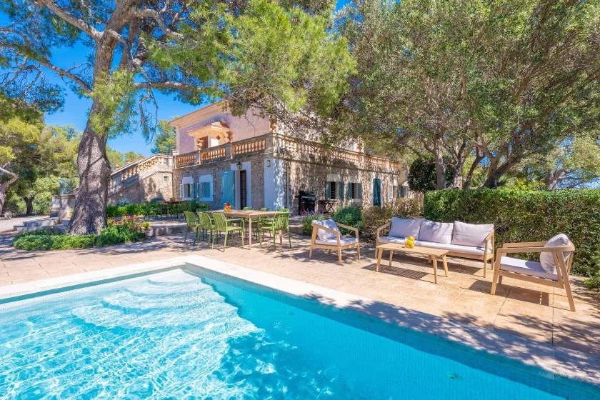 Una piscina junto a una zona de estar al aire libre y una casa frondosa.