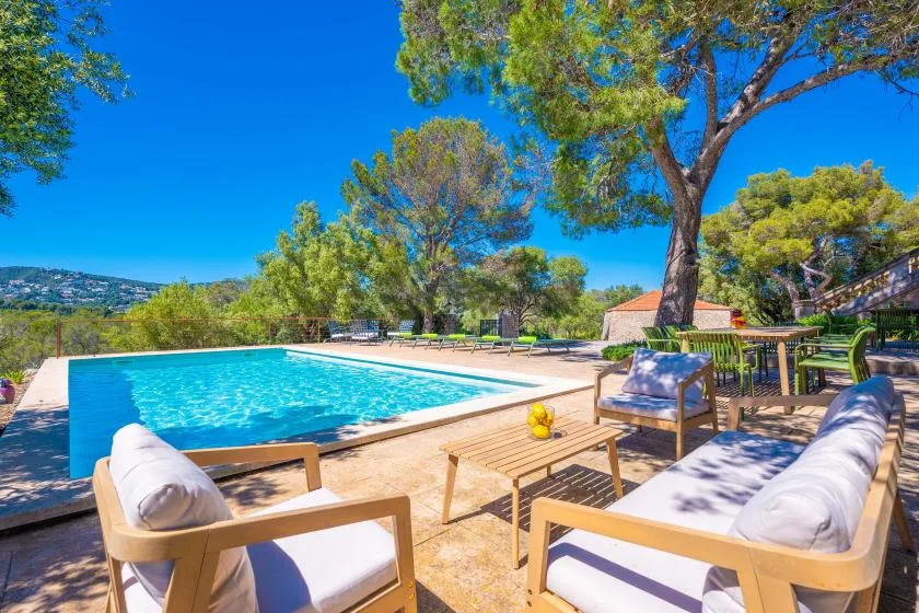 A sunny outdoor poolside seating area with loungers and trees.