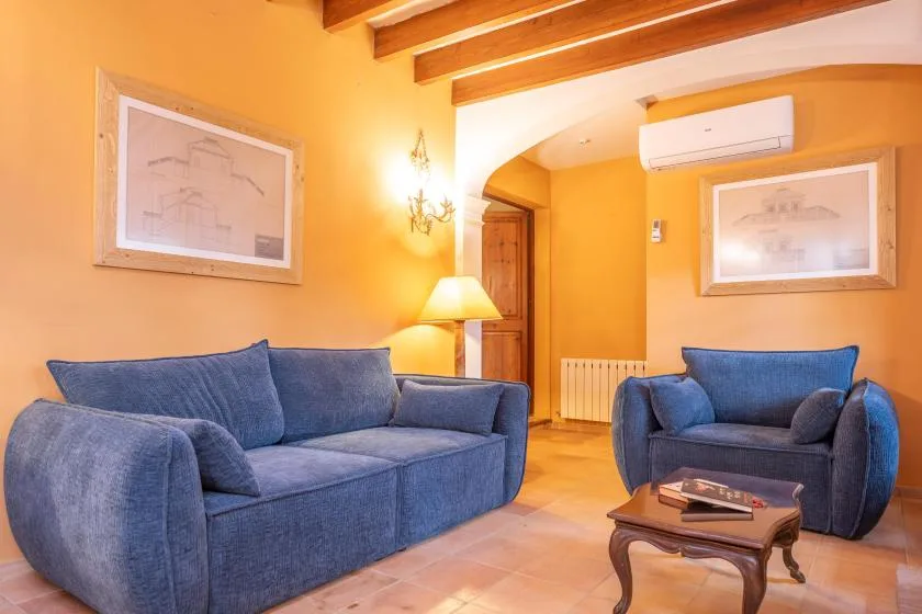 Una sala de tonos cálidos con asientos azules, una mesa de centro y vigas expuestas.