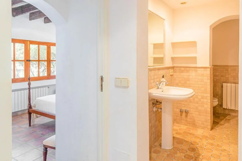 Un baño con lavabo de pedestal y una puerta abierta hacia un dormitorio.