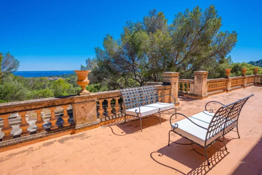 Una terraza soleada con asientos metálicos ofrece vistas a los árboles y al mar.