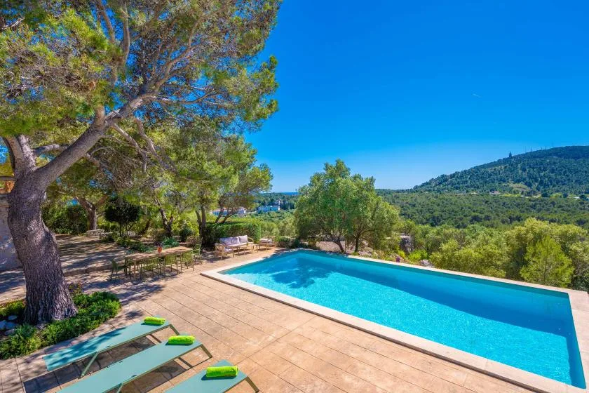 Una piscina al aire libre está en una terraza de baldosas con vistas a una colina verde.