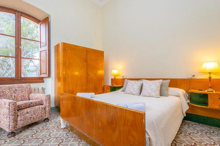 Un dormitorio con cama de madera, armario a juego y sillón estampado junto a la ventana.