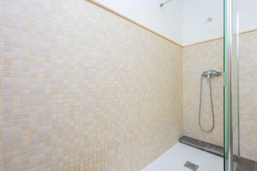 Una zona de ducha con azulejos, ducha de mano y panel de vidrio.