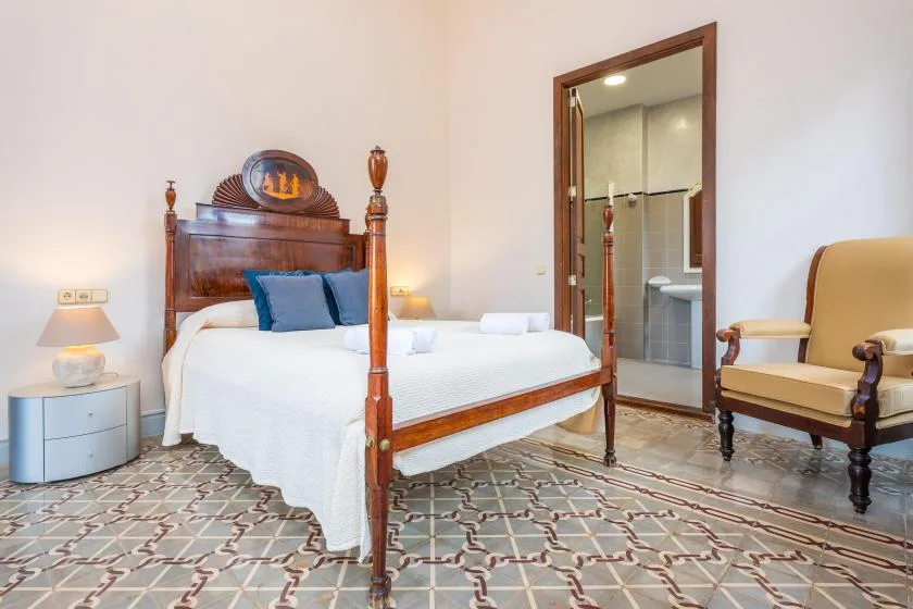 Un dormitorio con una cama de madera, suelo de baldosas estampadas y un baño contiguo.