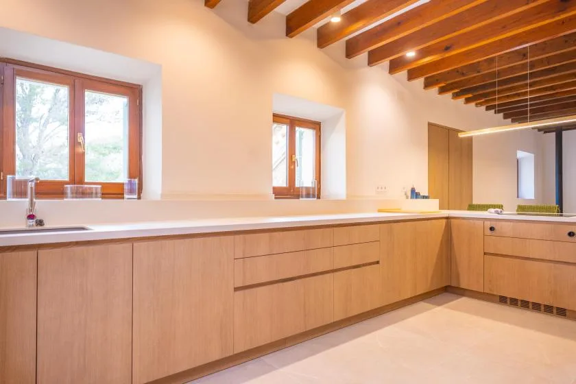 Una cocina moderna con gabinetes de madera clara y una larga encimera bajo vigas de madera vistas.
