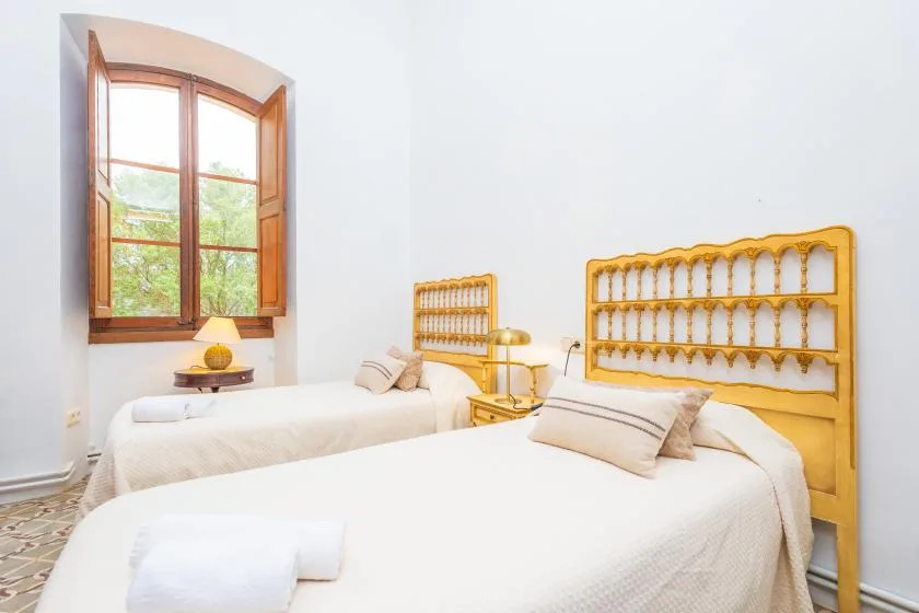 Un dormitorio luminoso con dos camas bajo una gran ventana con marco de madera.