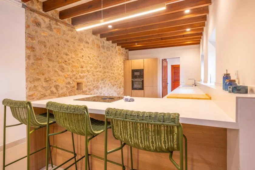 Una cocina con una barra larga, taburetes tejidos y vigas de madera a la vista.