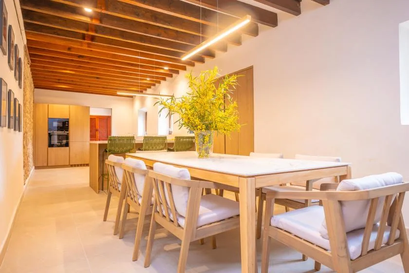 Comedor con una mesa larga y asientos acolchados bajo vigas de madera expuestas.