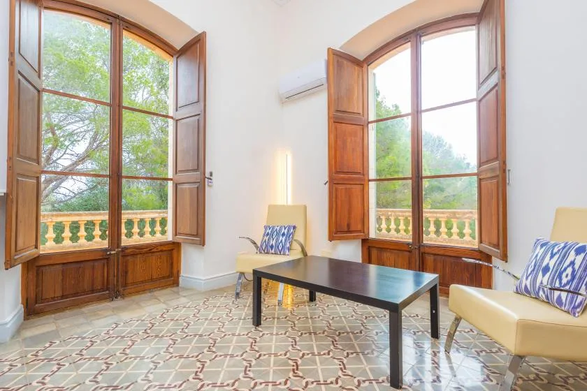 Una sala de estar luminosa con una mesa de centro oscura entre dos ventanas.