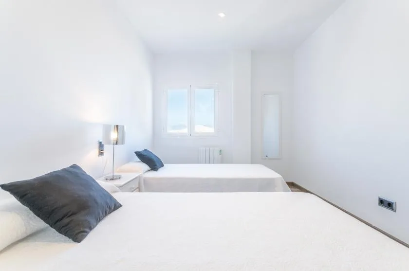 Un dormitorio luminoso con ropa de cama blanca y dos ventanas.