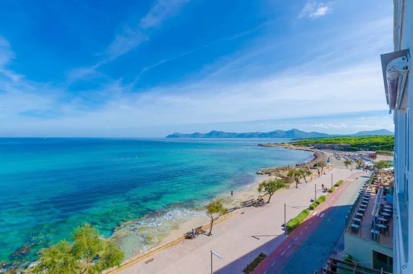 Un paseo costero bordea una playa de arena y un mar azul y transparente.
