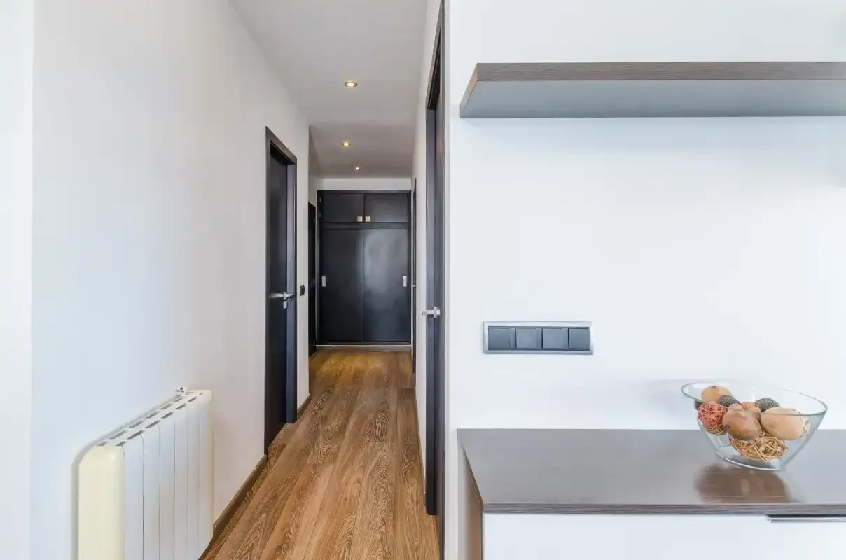 Un pasillo luminoso con suelo de madera y un radiador blanco.
