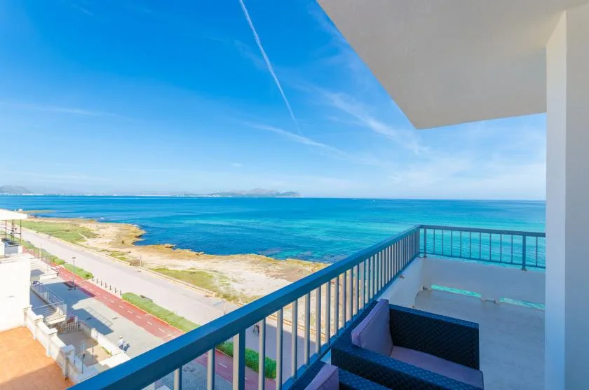 A balcony overlooks the blue sea and a coastal walkway.