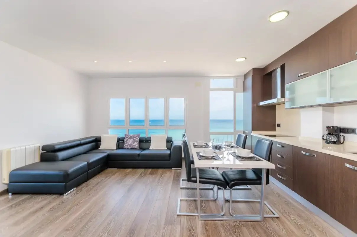 Una luminosa sala de estar y comedor con asientos, una mesa y vistas al mar por las ventanas.