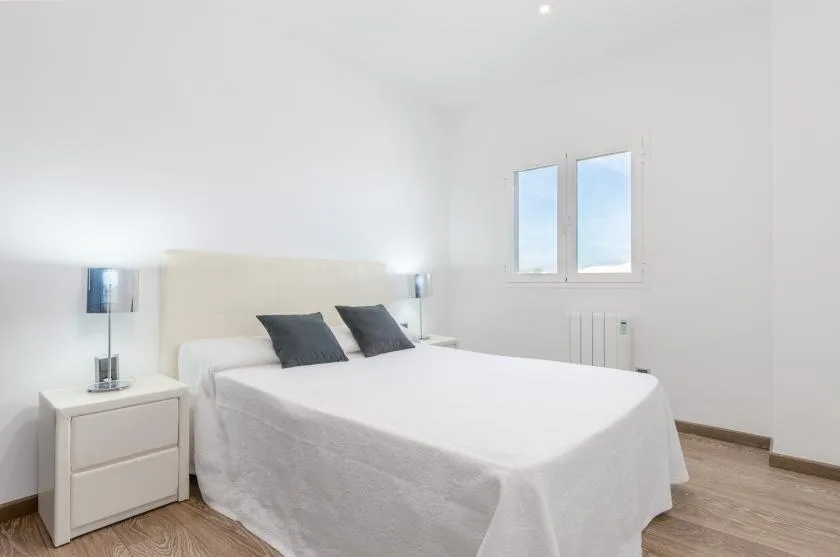 Un dormitorio luminoso con una cama bien tendida y dos ventanas.