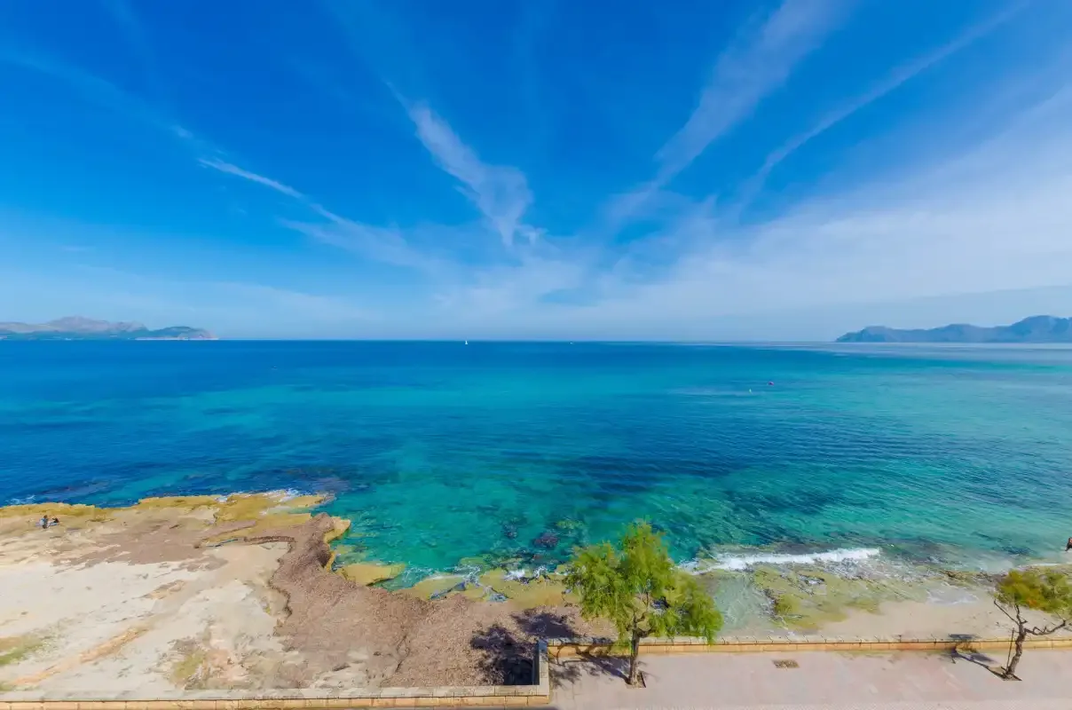 Una vista costera muestra aguas turquesas, una orilla rocosa y un cielo azul despejado.