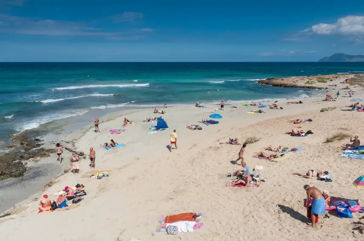 Una playa de arena con personas tomando el sol junto a olas turquesas.