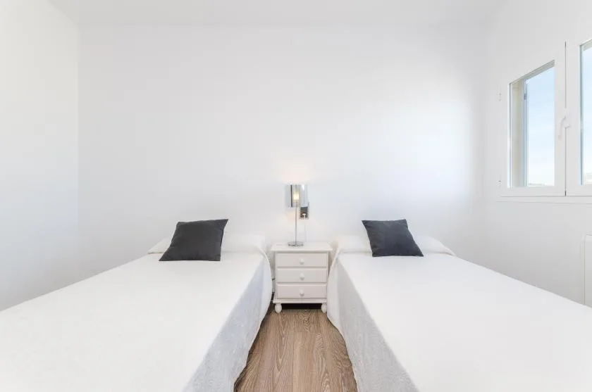 Un dormitorio luminoso con dos camas individuales y una mesita de noche.